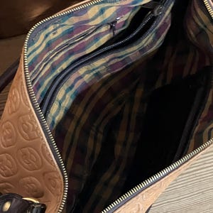 Pode incluir: Uma bolsa de m&atilde;o de couro castanho com um fecho de correr dourado e um forro de tecido estampado. A bolsa tem um design em relevo no exterior.