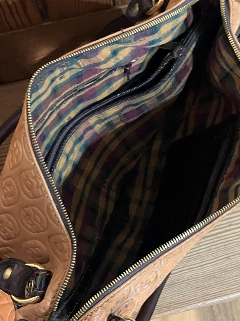 Pode incluir: Uma bolsa de m&atilde;o de couro castanho com um fecho de correr dourado e um forro de tecido estampado. A bolsa tem um design em relevo no exterior.