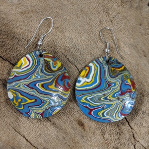 May include: A pair of teardrop-shaped earrings with a marbled pattern. The earrings feature a mix of blue, yellow, red, and white swirls. The earrings have silver-colored fish hook ear wires.