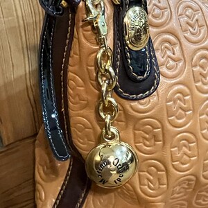 Pode incluir: Uma bolsa de m&atilde;o de couro bege com uma corrente dourada e um charme dourado que diz "Occhiali Made in Italy".