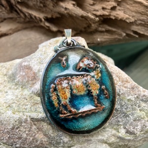 May include: A blue and brown ceramic pendant with a detailed image of a sheep. The pendant has a silver bail and is oval shaped.