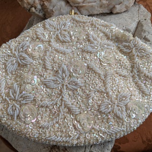 Puede incluir: Un bolso de mano blanco con cuentas y un dise&ntilde;o floral. El bolso est&aacute; cubierto de peque&ntilde;as cuentas y lentejuelas blancas.