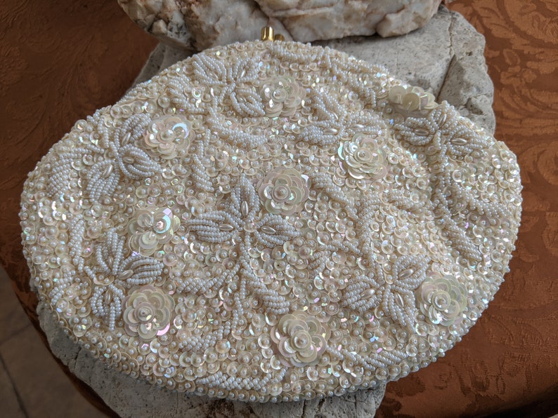 Puede incluir: Un bolso de mano blanco con cuentas y un dise&ntilde;o floral. El bolso est&aacute; cubierto de peque&ntilde;as cuentas y lentejuelas blancas.