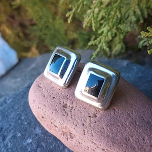 Puede incluir: Un par de pendientes cuadrados de plata con piedras de ónix negro en el centro.