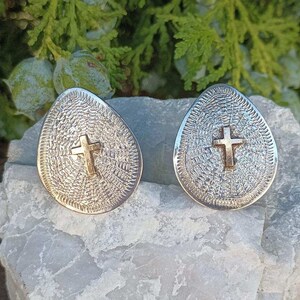 May include: A pair of silver teardrop-shaped earrings with a textured surface and a gold cross design.