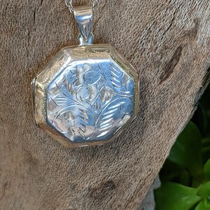 May include: A silver locket necklace with an intricate floral design. The locket is octagonal in shape and has a delicate chain.