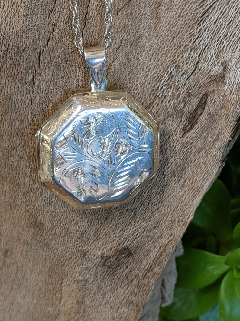 May include: A silver locket necklace with an intricate floral design. The locket is octagonal in shape and has a delicate chain.
