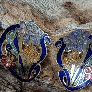 May include: A pair of blue and gold enamel earrings with a floral design. The earrings feature a stylized flower with blue, green, and gold accents.