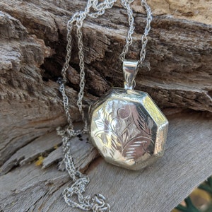 May include: A silver locket necklace with a detailed floral design. The locket is octagonal in shape and hangs from a delicate silver chain.