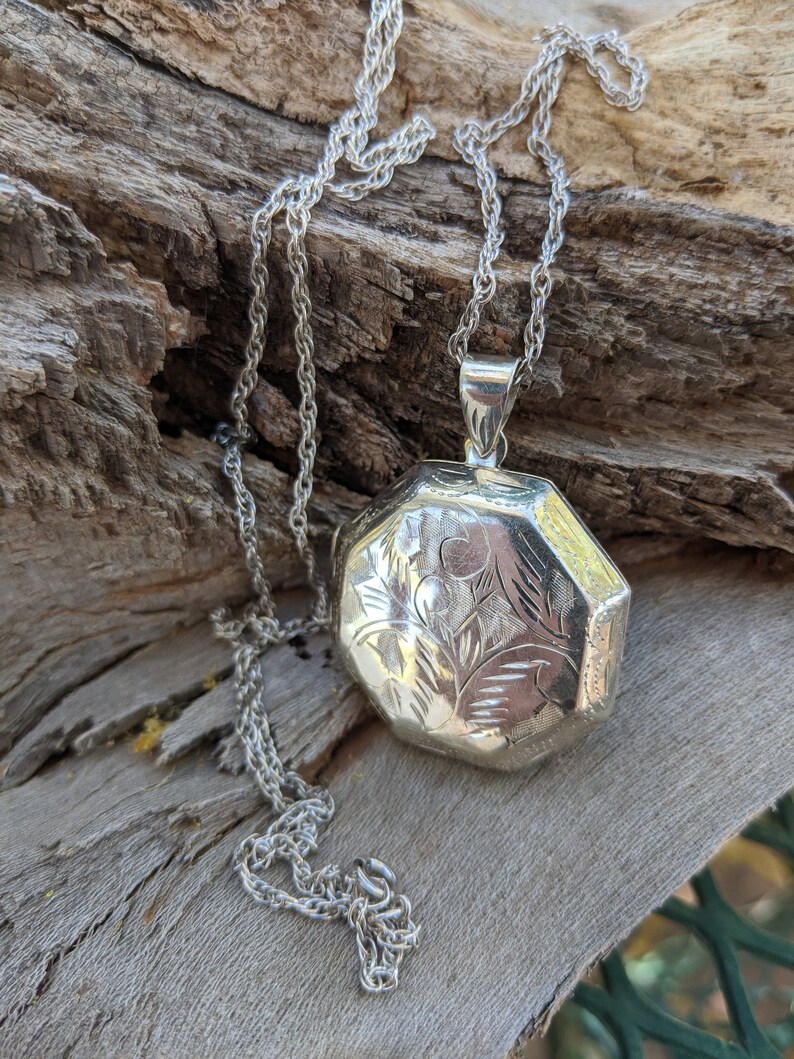 May include: A silver locket necklace with a detailed floral design. The locket is octagonal in shape and hangs from a delicate silver chain.