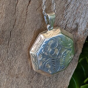 May include: A silver locket necklace with an octagonal pendant featuring an engraved floral design.