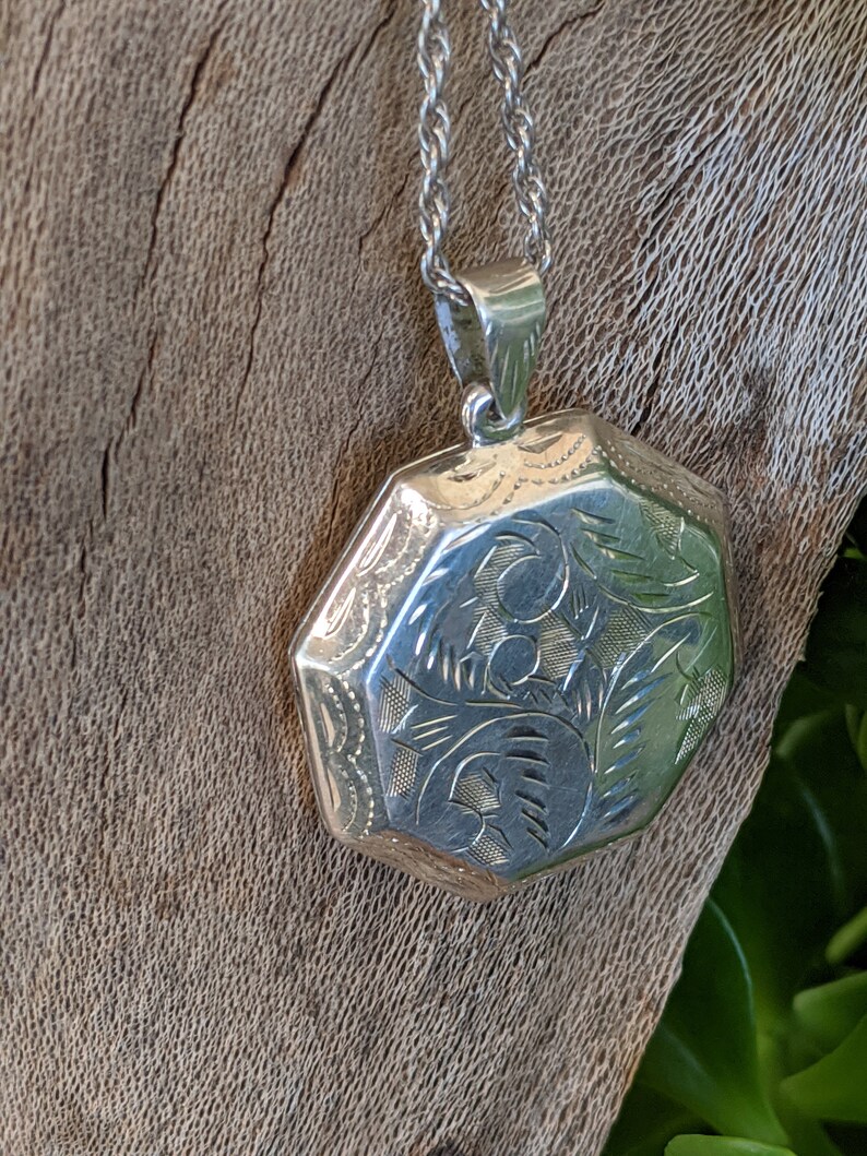 May include: A silver locket necklace with an octagonal pendant featuring an engraved floral design.