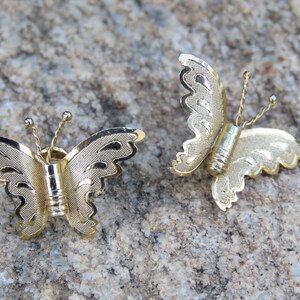 May include: A pair of gold butterfly earrings with intricate details. The butterflies have a delicate, filigree design and are a classic style.