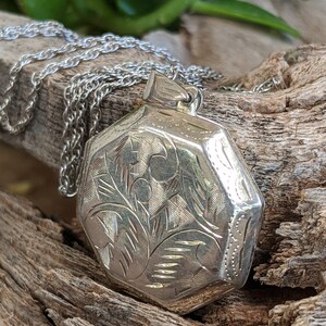 May include: A silver locket necklace with an octagonal pendant featuring an intricate floral design. The locket is on a silver chain.