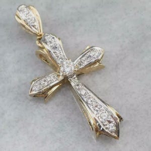 Puede incluir: Un colgante de cruz de oro y diamantes. La cruz presenta un diamante central y está adornada con numerosos diamantes más pequeños. El colgante tiene una argolla para sujetarlo a una cadena. El diseño es elegante y adecuado para fines religiosos o de moda.