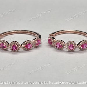 Puede incluir: Dos pulseras de oro rosa, cada una con piedras preciosas rosas en forma ovalada y de pera, rodeadas de piedras claras más pequeñas. Las pulseras se exhiben sobre una superficie blanca.