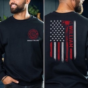 May include: Navy blue sweatshirt with a red and white Brawley Fire Dept logo on the front. The back features an American flag design with a red axe and the name "WILLIAM" in white. A patriotic themed apparel item.