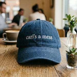 Puede incluir: Una taza de cerámica blanca con un asa negra y el texto "But First, Coffee" en un estilo manuscrito. La taza está sobre una superficie blanca. La taza mide aproximadamente 10 cm de alto.
