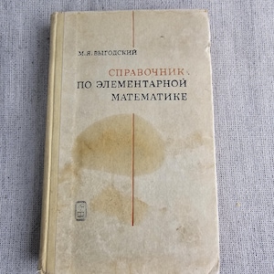 Puede incluir: Un libro antiguo con una cubierta beige, con el título "Справочник по элементарной математике" en ruso. La cubierta también incluye el nombre del autor, M.Ya. Vygodskiy, y un pequeño emblema. El libro muestra signos de edad con manchas y desgaste.