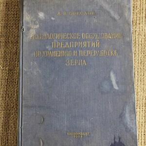 Puede incluir: Un libro azul vintage con letras doradas. El título está en ruso y el libro muestra signos de desgaste. La portada tiene manchas y una textura desgastada. El libro se titula "Equipamiento tecnológico de empresas para el almacenamiento y procesamiento de granos."