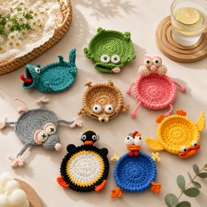 May include: A collection of colorful, handmade crochet coasters in various animal shapes, including a frog, penguin, and mouse. The coasters are made of yarn and feature detailed facial expressions and body parts. The coasters are designed to hold a glass or cup.