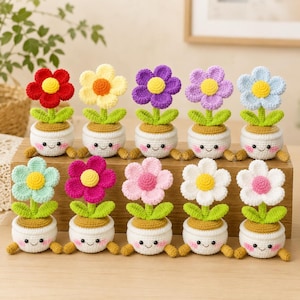 May include: Ten small crocheted potted flowers arranged in two rows. Each white pot features a smiling face with pink cheeks and two small feet. The flowers have vibrant petals in red, yellow, purple, lavender, blue, mint, magenta, pink, and white.