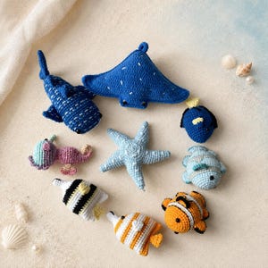 May include: A collection of nine crocheted sea creatures including a blue whale shark, a blue stingray, a light blue starfish, a pink seahorse, a blue and white fish, a black and white striped fish, a yellow and white striped fish, and an orange clownfish.