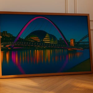May include: A framed print depicting a night scene of a bridge with a pink arch and city lights reflected in the water. The artwork is displayed on a wooden floor, leaning against a wall.