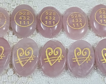 Puede incluir: Diez piedras ovaladas de cuarzo rosa. Cinco piedras tienen texto dorado con los números 528, 432 y 111. Las otras cinco piedras tienen un diseño de corazón dorado con líneas y puntos.