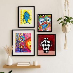 Puede incluir: Cuatro impresiones artísticas enmarcadas con marcos negros se exhiben en una pared blanca. El arte incluye un pez azul, dos caras de payaso, una escena abstracta colorida y un jarrón en blanco y negro. También se ve un colgador de plantas de macramé con una planta verde.