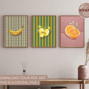 Puede incluir: Tres impresiones artísticas enmarcadas con ilustraciones de frutas. La primera impresión presenta un plátano sobre un fondo a cuadros verde y beige. La segunda impresión muestra limones sobre un fondo a rayas amarillas y turquesas. La tercera impresión muestra rodajas de naranja sobre un fondo a rayas rojas y blancas.