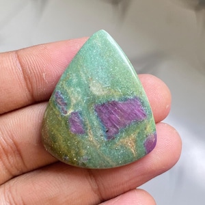 May include: A polished, teardrop-shaped gemstone with a green base color and vibrant magenta inclusions. The stone has a smooth, glossy surface, and the magenta patterns create a striking contrast against the green background. This gemstone is ideal for jewelry making.