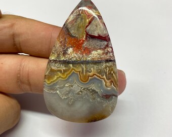 May include: A polished, teardrop-shaped gemstone. The stone displays a variety of colours, including red, orange, yellow, grey, and brown, with complex patterns and layers. The top has a pointed tip, and the bottom is rounded, creating a smooth finish.