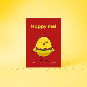 Könnte beinhalten: Eine rote Grußkarte mit dem Text "Happy me!" zeigt ein Cartoon-Küken, das als Hamburger verkleidet ist. Das Küken ist gelb mit einem Burger-Patty und Salat. Ein kleines rotes Herz befindet sich über dem Kopf des Kükens.