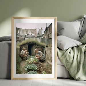 May include: A framed print shows children gardening in a vintage scene. The image features a brick structure with a grassy roof, a clothesline with washing, and buildings in the background. The children are tending to a garden with cabbages and other plants.