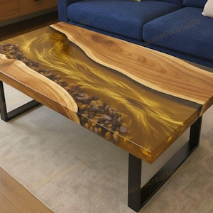 Könnte beinhalten: Rechteckiger Couchtisch mit Holzplatte und schwarzen Metallbeinen. Der Tisch hat einen Fluss aus goldenem Harz und Steinen, der durch die Mitte verläuft und von Naturholz umrahmt wird.