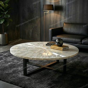 Könnte beinhalten: Ein runder Couchtisch mit einer Mosaik-Oberfläche in Weiß- und Grautönen, getragen von schwarzen Metallbeinen. Der Tisch steht in einem modernen Wohnzimmer mit einem schwarzen Ledersofa und einer Stehlampe. Der Tisch hat einen Durchmesser von ca. 120 cm.