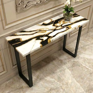 May include: A rectangular console table with a white marble top featuring black and gold veining. The table has a black metal frame and is suitable for entryways or living rooms. A vase of white flowers sits on the table.