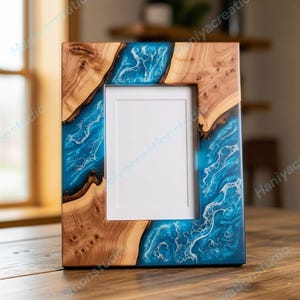 Puede incluir: Marco de fotos de madera con una abertura rectangular. El marco presenta un diseño único con madera natural y una vibrante resina azul, creando un efecto fluido similar al océano. El marco se muestra sobre una superficie de madera.