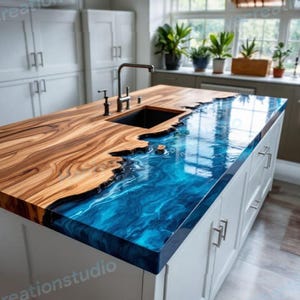 Puede incluir: Una isla de cocina con un diseño de encimera único. La encimera presenta una combinación de madera natural y resina epoxi azul que se asemeja a las olas del océano. La isla tiene una base blanca con puertas y cajones de armario, y un fregadero negro.