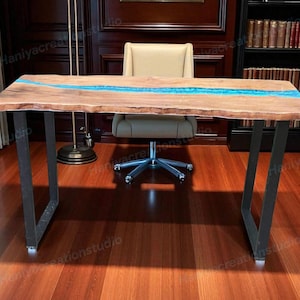 May include: A wooden desk with a live edge and a blue resin river. The desk has black metal legs and is set in a home office. The desk is approximately 152 cm long.