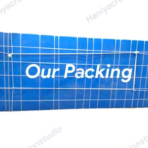 Puede incluir: Un paquete azul con un patr&oacute;n de cuadr&iacute;cula y las palabras "Our Packing" en blanco. El paquete est&aacute; asegurado con una cuerda blanca. El tema general es el embalaje y el env&iacute;o.