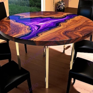 May include: A circular dining table featuring a purple and blue resin river design set within a wooden surface. The table has gold-coloured legs and is surrounded by black chairs. The table's diameter is approximately 120 cm.