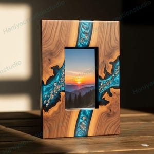 Pode incluir: Uma moldura retangular de madeira com uma foto de paisagem. A moldura é feita de madeira escura com detalhes em resina turquesa e flocos de prata. A foto mostra um pôr do sol sobre as montanhas.