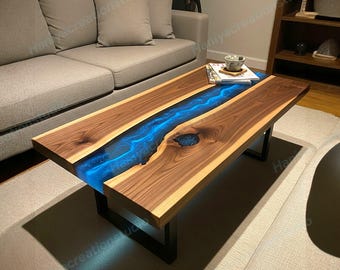 May include: A rectangular coffee table featuring two natural walnut wood slabs with a live edge, separated by a central glowing blue resin river. The table is supported by black metal legs and includes a small knot filled with blue resin.