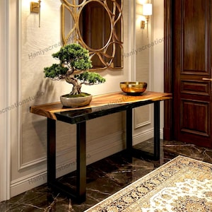 May include: A rectangular console table featuring a natural wood grain top with a dark resin edge, supported by black metal legs. A green bonsai tree in a ceramic pot and a gold-toned metal bowl are placed on the surface of the table.