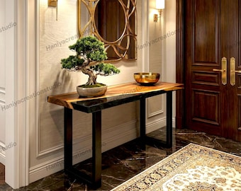 Puede incluir: Una mesa consola rectangular con una superficie de madera natural con un borde de resina oscura, sostenida por patas de metal negro. Un bonsái verde en una maceta de cerámica y un cuenco de metal dorado se encuentran sobre la mesa.