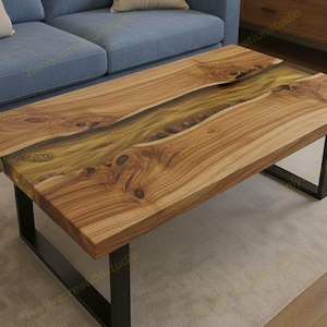 Op de afbeelding: Een rechthoekige houten salontafel met een live edge design. Het tafelblad is gemaakt van lichtbruin hout met een rivier van goudkleurige epoxyhars in het midden. De tafel heeft zwarte metalen poten. Ongeveer 120 cm lang.