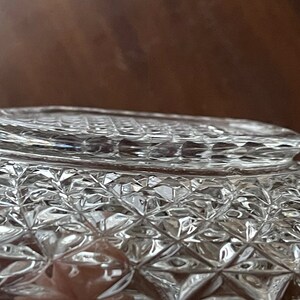 May include: Close-up of a clear, cut-glass bowl with a diamond pattern. The bowl's rim has a textured design. The glass reflects light, creating a sparkling effect. The bowl is likely for serving or display.