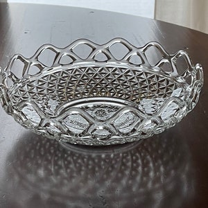 May include: A clear, oval-shaped glass serving bowl with a diamond-cut pattern and a decorative openwork rim. The bowl is designed with a scalloped edge and sits on a dark wooden surface. This elegant piece is suitable for serving fruit or decorative purposes.